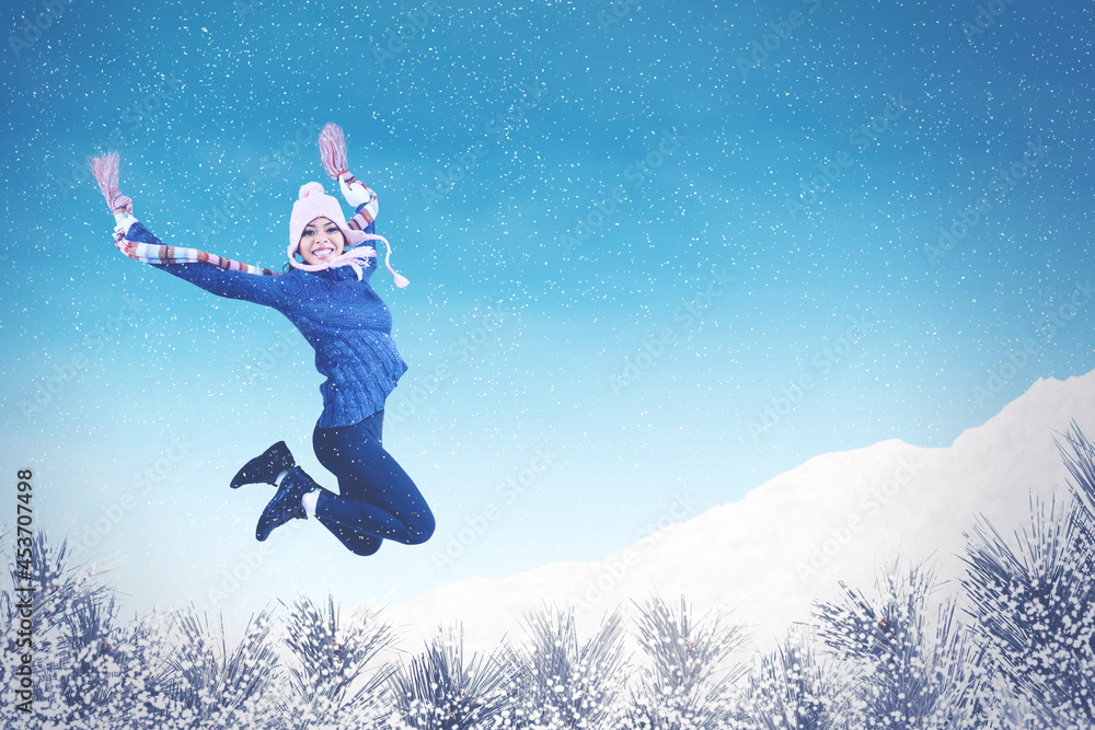Excited young woman jumping under snowfall at park Excited young woman jumping under snowfall at park