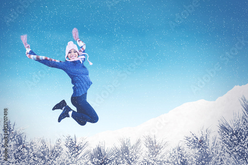 Excited young woman jumping under snowfall at park