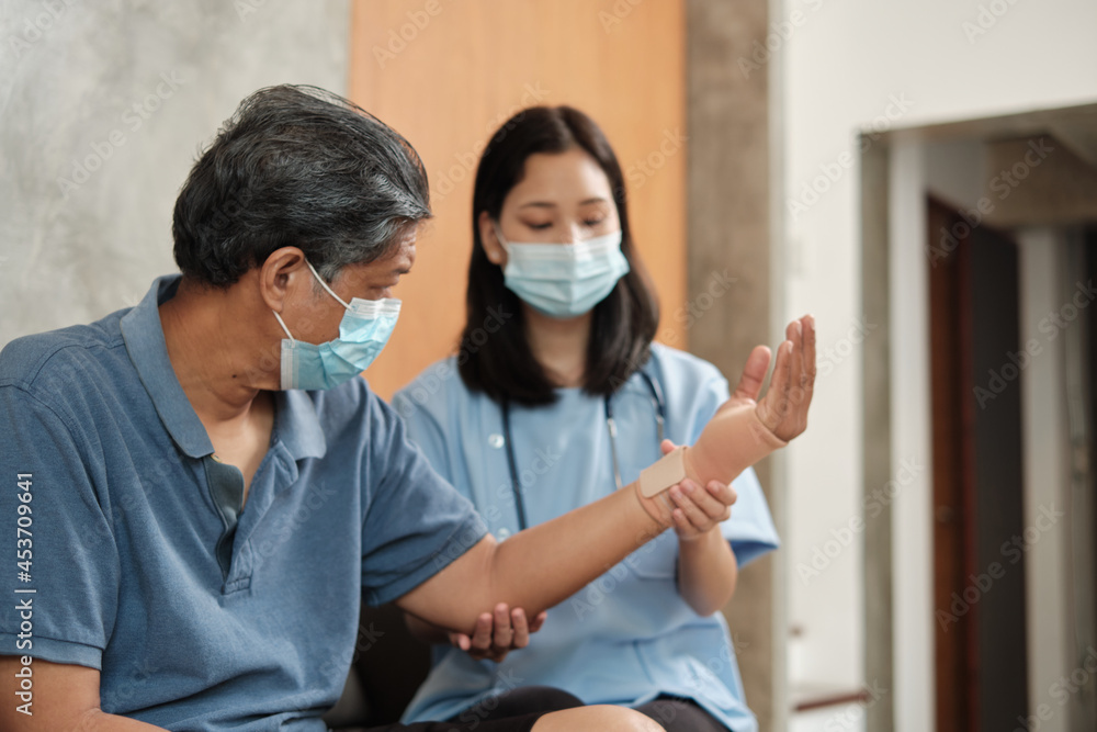 Asian female doctor with face mask health exam on elderly male patients, helping to do physical therapy treatment on injured arm. Home medical services are available to retired seniors.