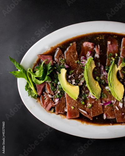Mexican food, fish fajitas over a sauce, accompanied by avocado