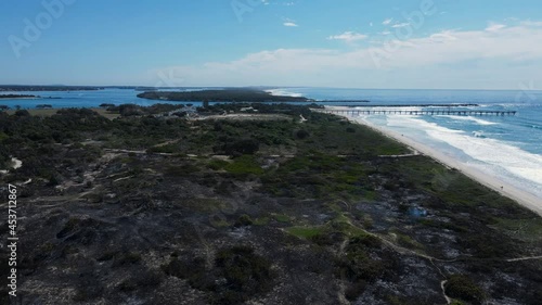 Charred remains of a coastal fire along the sand dunes of a popular holiday spot. Moving drone view photo