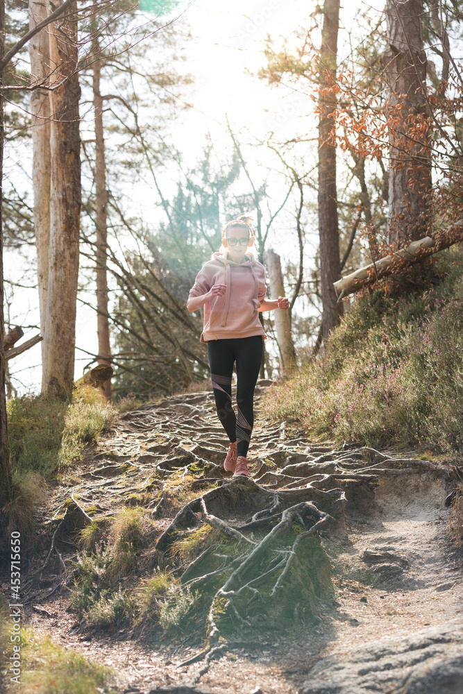 Active sporty woman listening to the music while running in autumn fall forest. Female runner training outdoor. Healthy lifestyle image of young caucasian woman jogging outside
