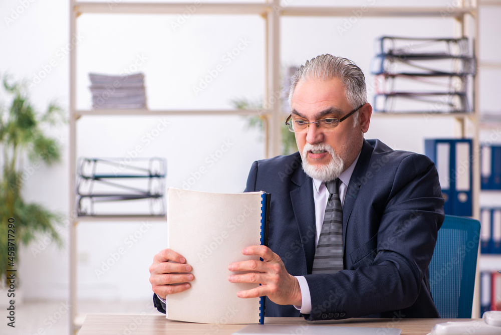 Old male employee unhappy with excessive work in the office Old male employee unhappy with excessive work in the office