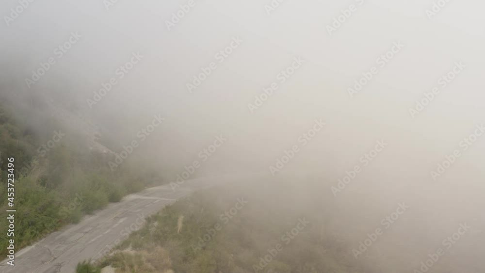 Drone view of windy road on side of mountain vanishing into clouds. Aerial view of a mountain road in San Gabriel Mountains in Southern California in foggy weather. Abandoned CA-39. Drone view of windy road on side of mountain vanishing into clouds. Aerial view of a mountain road in San Gabriel Mountains in Southern California in foggy weather. Abandoned CA-39.
