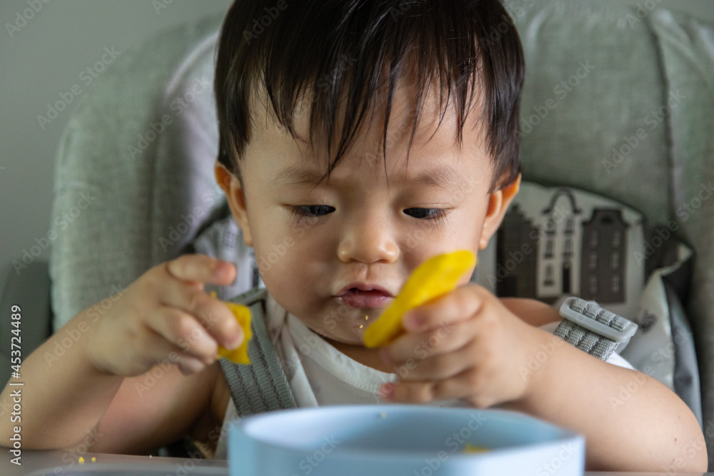 adorable and cute happy Asian Chinese baby boy siting on baby chair enjoying his lunch adorable and cute happy Asian Chinese baby boy siting on baby chair enjoying his lunch