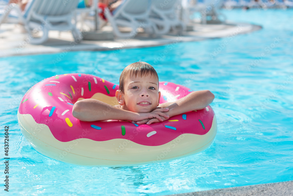 Happy little boy with variegated life ring in the form of a donut has fun in the swimming pool