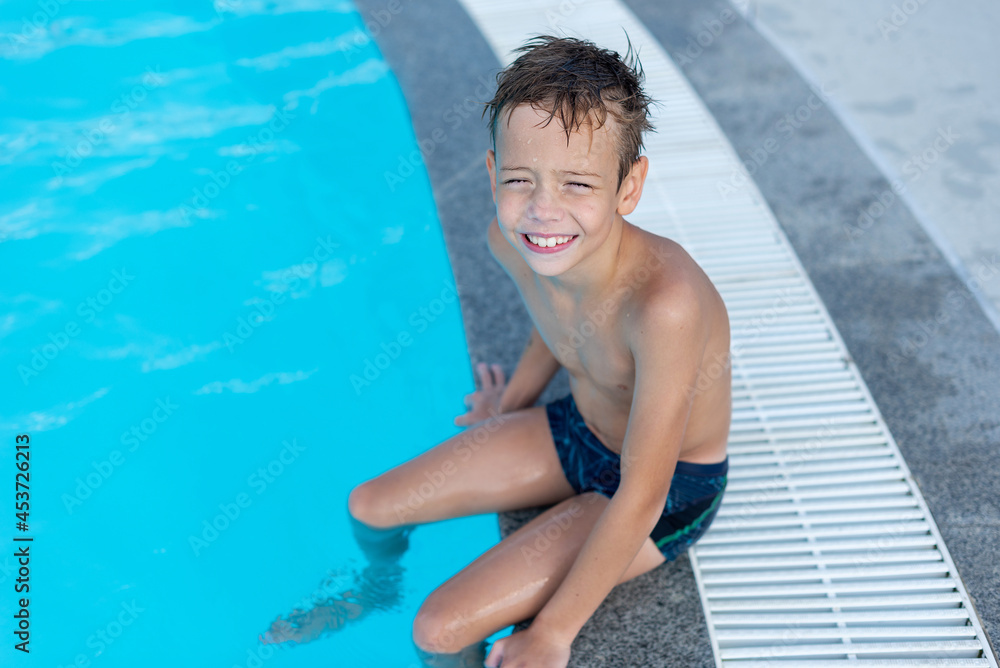 The boy on the side of the pool is smiling. The open air swimming pool.