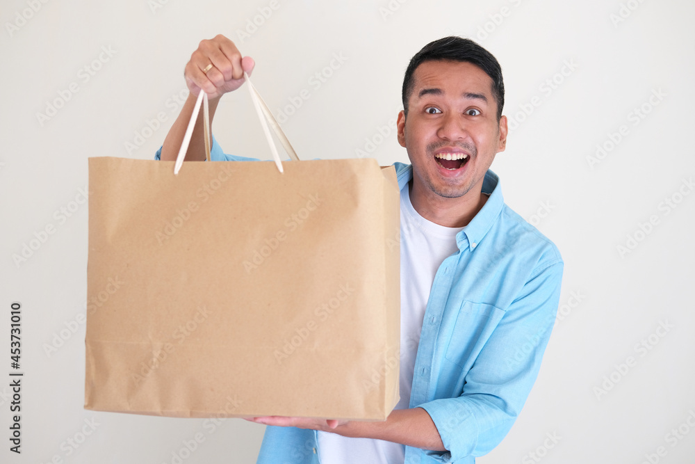 Adult Asian man showing happy face expression while showing his big shopping bag Adult Asian man showing happy face expression while showing his big shopping bag