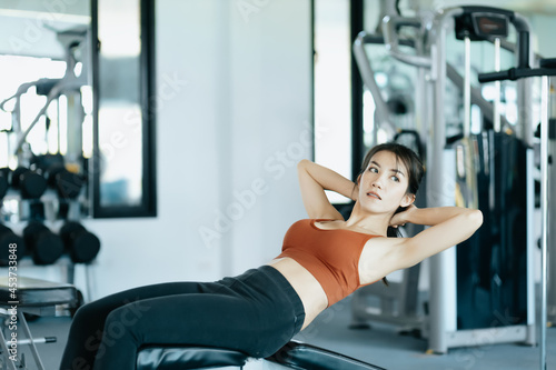 Asian woman in sportswear training sit up at fitness gym. Fitness and workout concept.