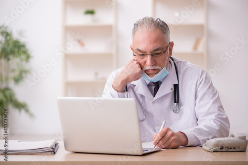 Old male doctor working in the clinic during pandemic