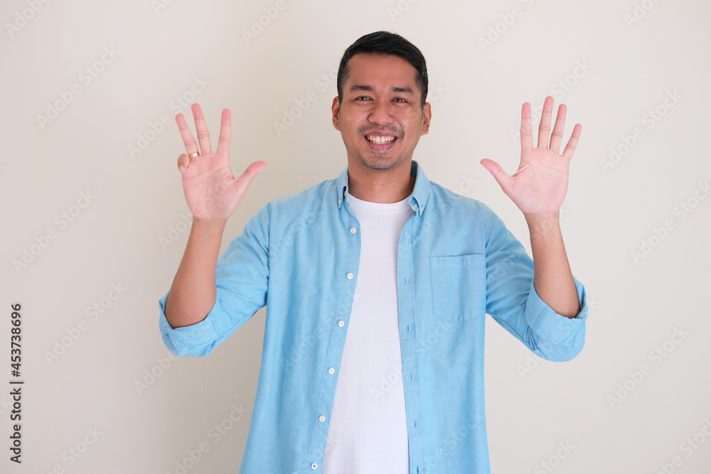 Asian man smiling happy while giving nine finger up symbol Asian man smiling happy while giving nine finger up symbol