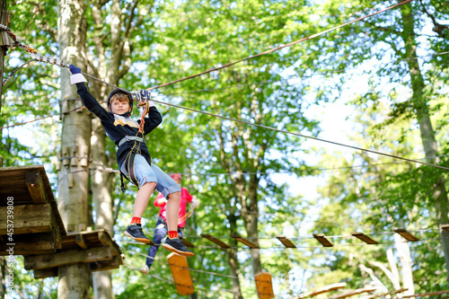 Child in forest adventure park. Kid boy in helmet climbs on high rope trail. Agility skills and climbing outdoor amusement center for children. Outdoors activity for kids and families.
