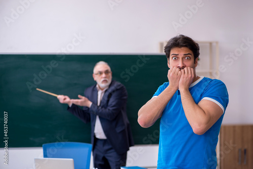 Old male teacher and young male student in front of blackboard