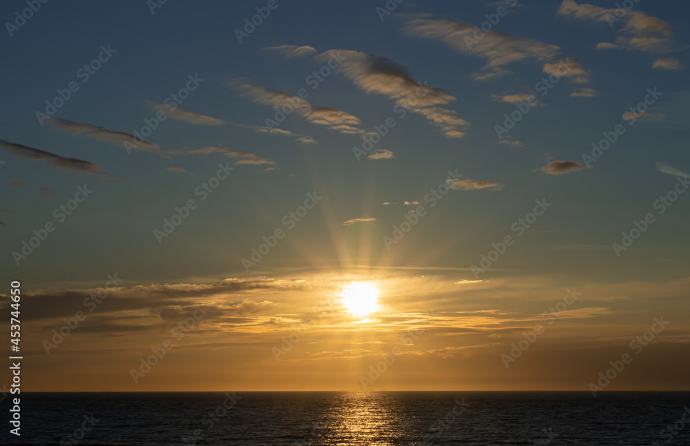 Zachodzące słońce, chowające się za horyzontem morza na tle przepięknych chmur i kolorystycznego niebieskiego nieba