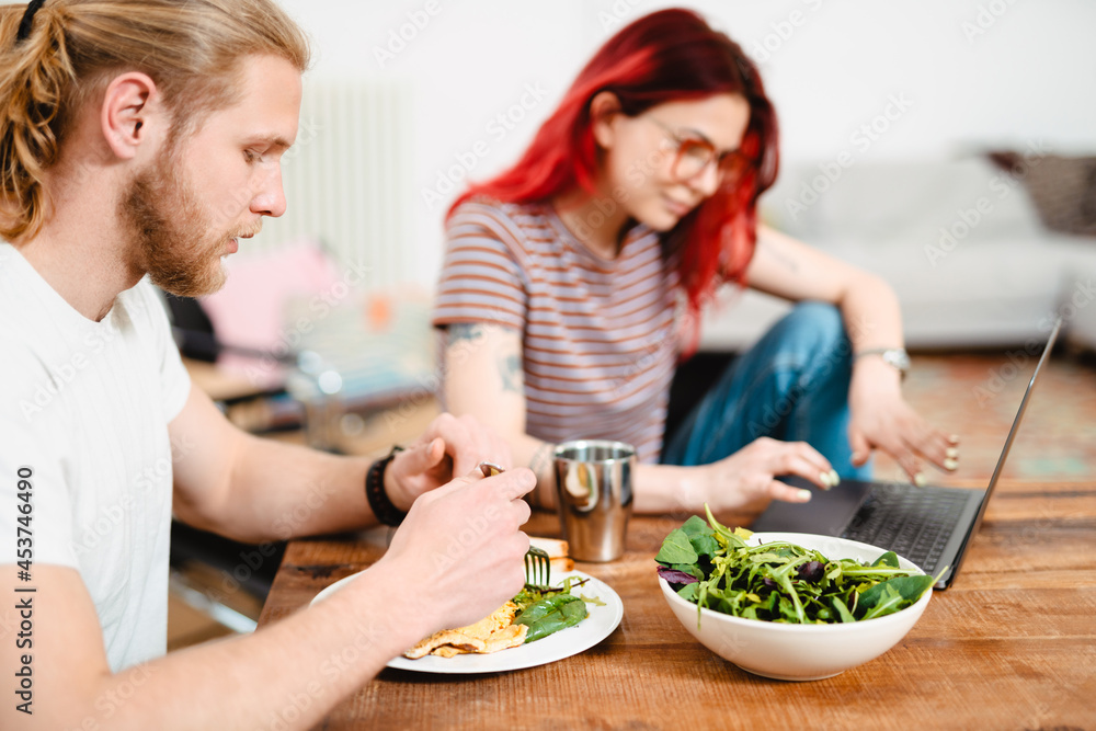 Young white couple using laptop and having lunch while sitting at table Young white couple using laptop and having lunch while sitting at table