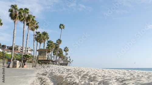 Tropical palm trees, white sandy beach by sea water wave, pacific ocean coast, San Clemente California USA. Blue sky and lifeguard tower. Life guard watchtower hut, summertime shore. Los Angeles vibes
