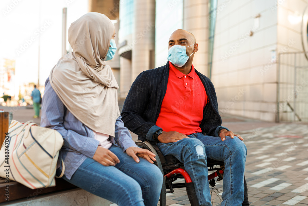 Muslim woman and disabled man wearing face mask talking to each other Muslim woman and disabled man wearing face mask talking to each other
