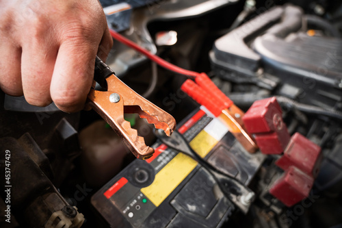 The mechanic connects the clamps to the discharged car battery.