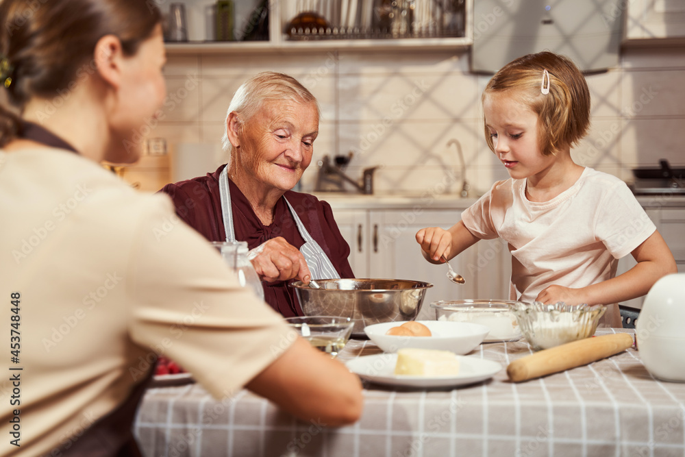 Pensioner mixing up dough with girl adding flour