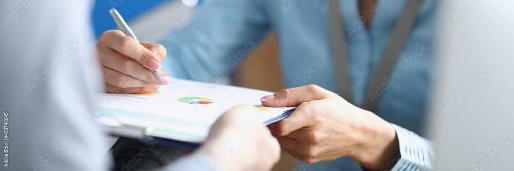 Businesswoman signing document on clipboard in hands of secretary closeup