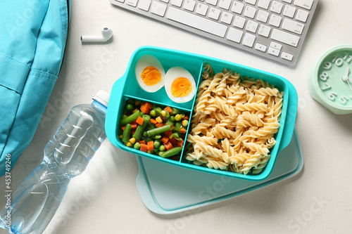 Lunch box with tasty food, bottle of water, alarm clock and keyboard on light background