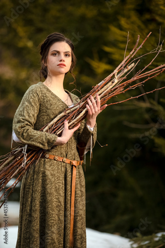 Young Brunette Caucasian Housewife Posing in Spring Forest With Bunch of Firewoods in Hands Outdoors.