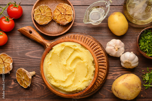 Bowl of tasty mashed potatoes with garlic and vegetables on wooden background