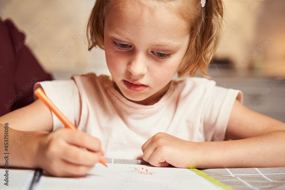 Concentrated kid using orange marker for painting picture Concentrated kid using orange marker for painting picture