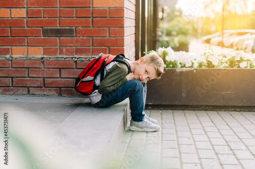 Back to school. Cute child with backpack, holding notepad and training books. School boy pupil with bag. Elementary school student going to classes. Kid sitting on stairs outdoors at brick wall.