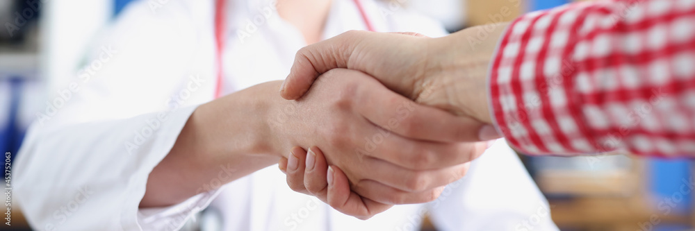 Woman doctor shaking hand of patient in clinic closeup Woman doctor shaking hand of patient in clinic closeup