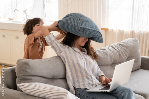 фотографія Angry mother try to work from home sitting with laptop on couch in living room with little son hitting her pillow