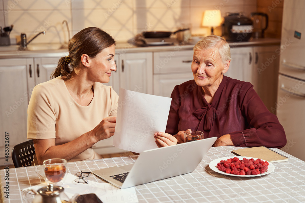 Female holding document and letting elderly woman have a look Female holding document and letting elderly woman have a look