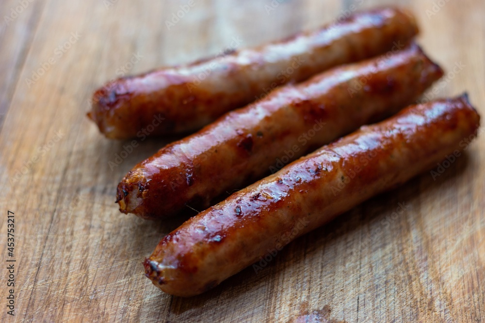 Three freshly fried sausages lie diagonally on a wooden board. Fat protruding is visible
Three freshly fried sausages lie diagonally on a wooden board. Fat protruding is visible