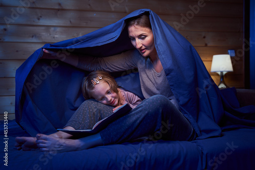 Female and child hiding under blanket while reading
