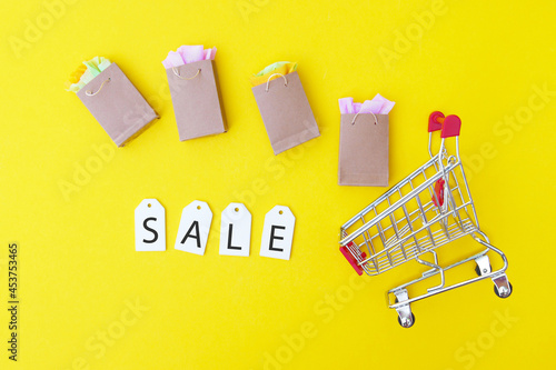 Shopping cart with paper bags and white labels with the word SALE on a yellow background.
