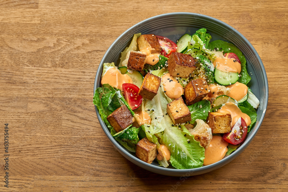 Diet salad with fried tofu, yellow sauce and vegetables in a bowl on a wooden background Diet salad with fried tofu, yellow sauce and vegetables in a bowl on a wooden background