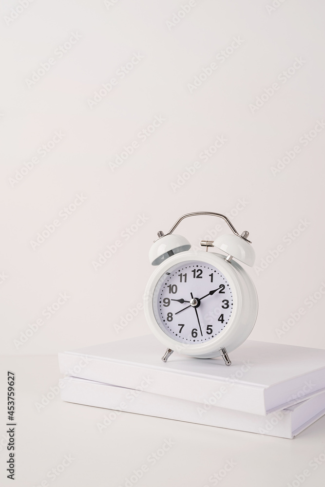 Naklejka premium White alarm clock on stack of books, mockup design