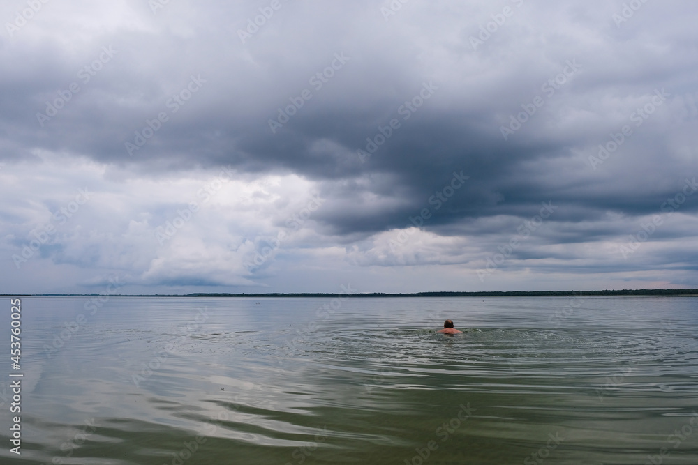 A lonely man swims in the deepest Lake Svitiaz, Volyn, Ukraine before the rain in Ukraine. Circles on the water. Offseason. Copy space.