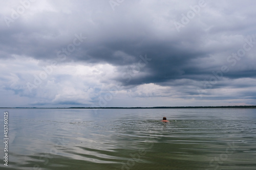 A lonely man swims in the deepest Lake Svitiaz, Volyn, Ukraine before the rain in Ukraine. Circles on the water. Offseason. Copy space.
