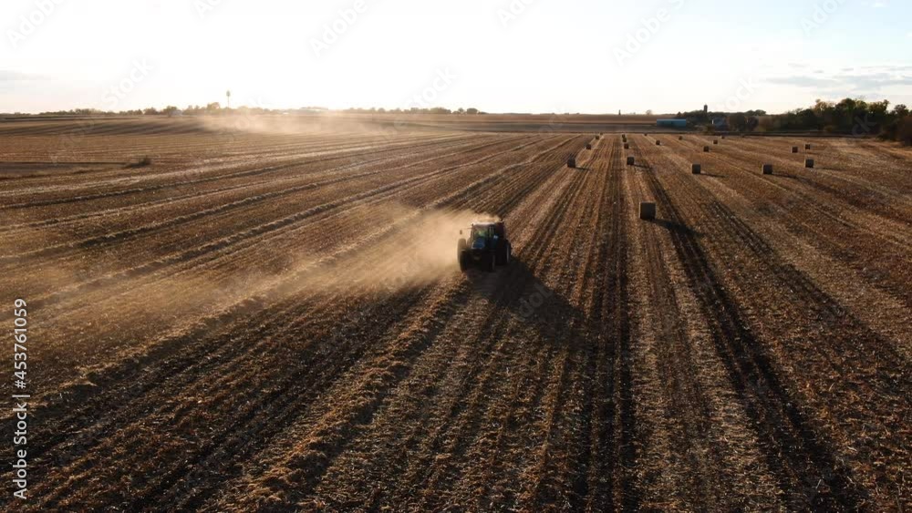 Tractor harvesting hay and producing hay bales in vast field during sunset. Tractor harvesting hay and producing hay bales in vast field during sunset.