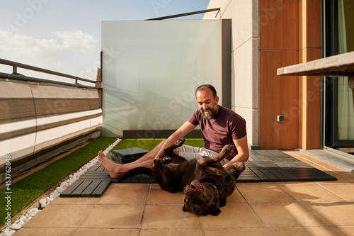 smiling middle-aged man playing with his dog while setting up a new floor on his terrace