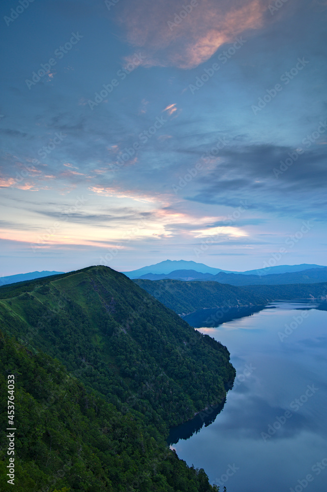 雄大な夜明けの空を湖面に映す山間の湖。日本の北海道の摩周湖。