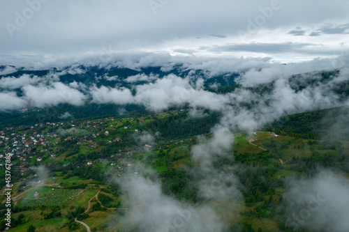 Rainy weather in a small town in mountains. Misty fog blowing over pine tree forest and country road. Aerial footage of spruce forest trees on the mountain hills at misty day. Morning fog at beautiful