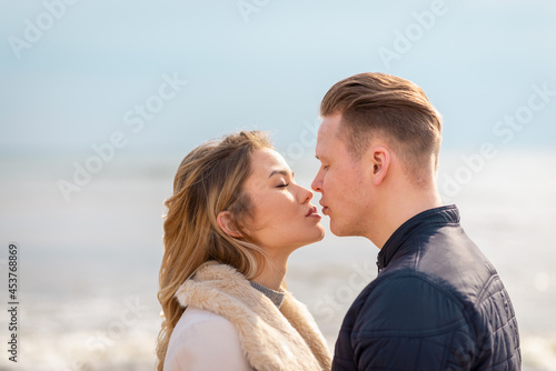 Young couple kissing outdoor.Stunning outdoors portrait of young stylish fashion couple posing in autumn sea background.