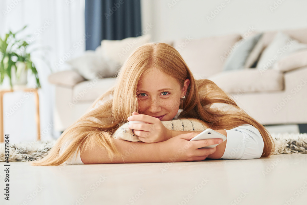 With smartphone in hands. Female teenager with blonde hair is at home at daytime With smartphone in hands. Female teenager with blonde hair is at home at daytime