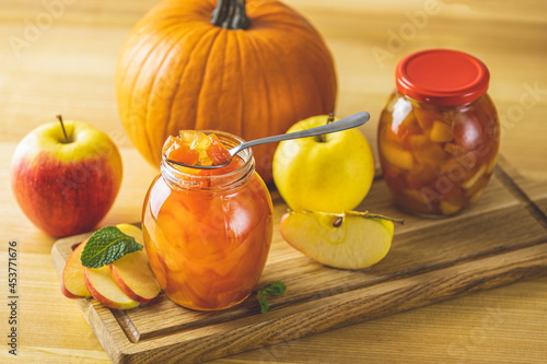 Fresh homemade pumpkin apple marmalade jam in glass jar on a wooden background. Several fresh apples, pumpkin and mint are near it