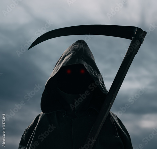 Death with a scythe stands against the background of a gloomy sky. photo