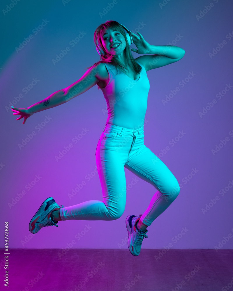 Portrait of young beautiful girl isolated on blue studio background in neon light filter. Concept of human emotions, facial expression, youth, sales, ad.