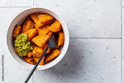 Baked sweet potato wedges with basil pesto in white bowl. Healthy vegan food concept.