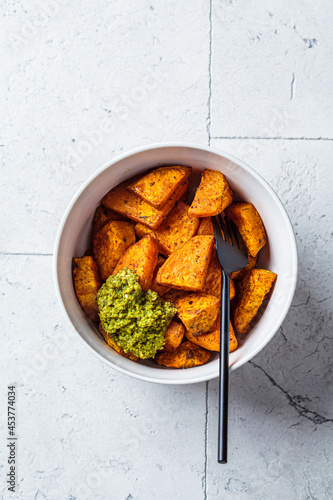 Baked sweet potato wedges with basil pesto in white bowl. Healthy vegan food concept.
